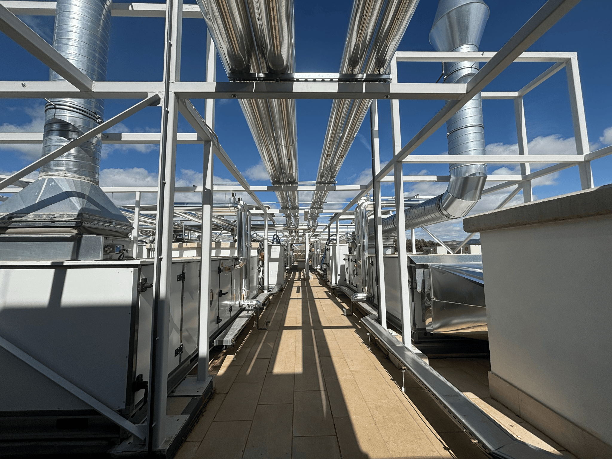 Instalación técnica exterior con conductos metálicos elevados, equipos de climatización y estructura de soporte vistos desde una pasarela central.